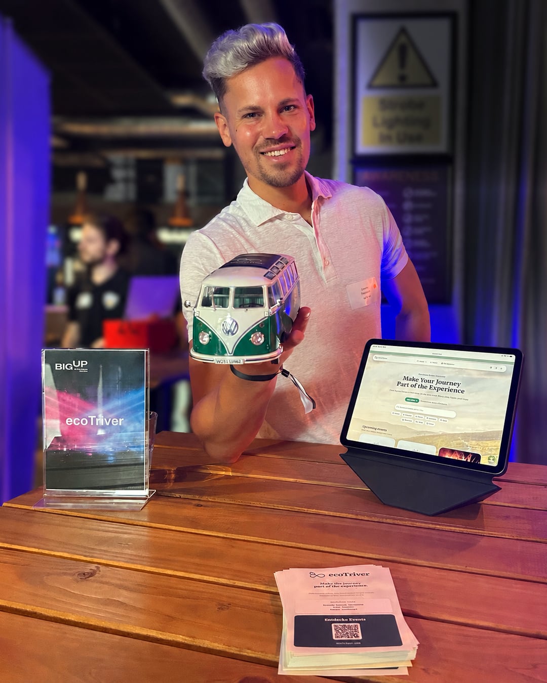 Dominic Thormann at the ecoTriver booth at the BIG UP Startup Summit, with tablet demo and VW bus model